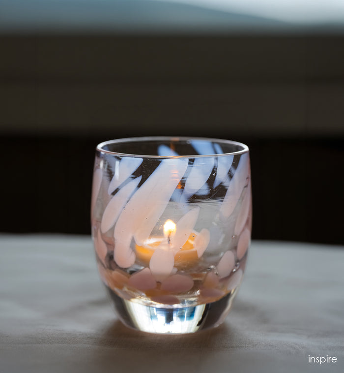 Glass candle holder with a lit candle inside on a reflective surface.