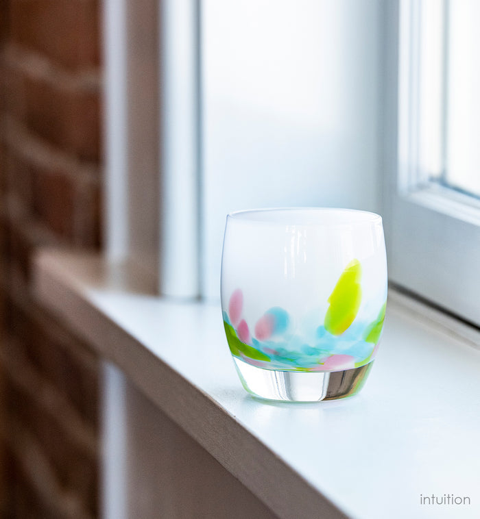 intuition blue, green and pink petals of color at the base of a white, hand-blown glass votive candle holder