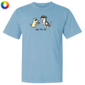 A light blue short-sleeve crewneck t-shirt featuring a cartoon graphic of two dogs shaking hands with the text 'just the tip' underneath. A small multicolor color wheel icon is visible in the top-left corner.