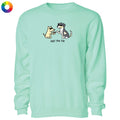 A mint green crewneck sweatshirt featuring a cartoon graphic of a yellow dog and a black-and-white cat shaking paws with the text 'Just the tip' underneath. A small multicolor color wheel icon is visible in the top-left corner.