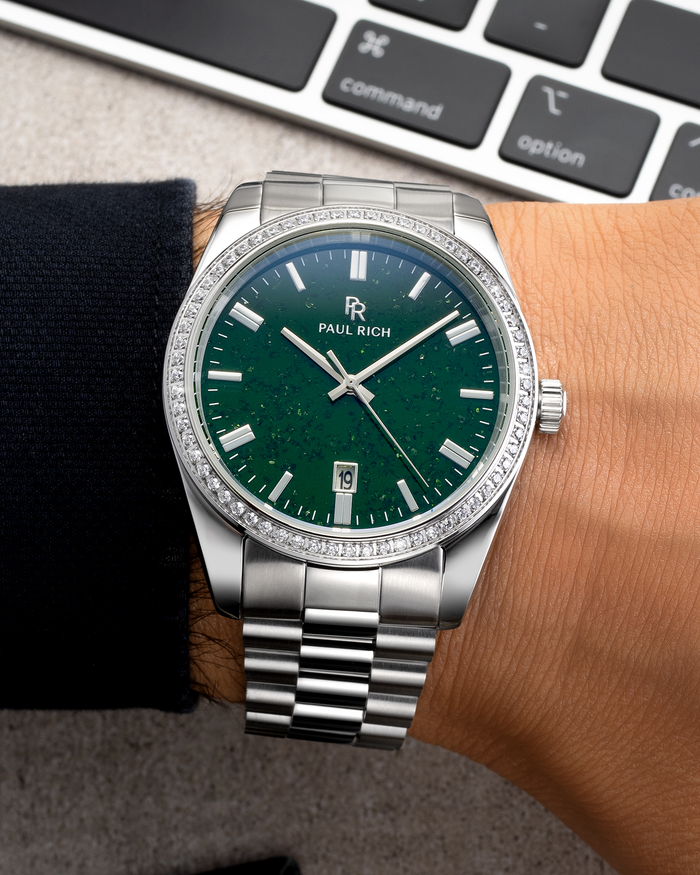 Silver wristwatch with a green aventurine dial, crystal-set bezel, and metal bracelet worn on a wrist near a keyboard on a desk surface.