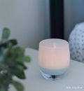 little boy blue, soft blue hand-blown glass votive candle holder on white table next to green plant.