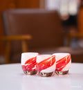 three maverick white with red wing, hand-blown glass votive candle holders  on a white table with brown leather chair in background.