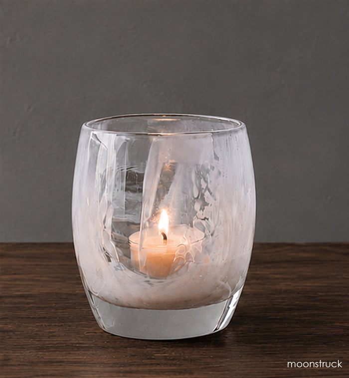 Clear glass candle holder with a lit candle on a wooden surface and dark background