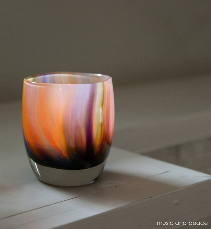 music and peace, rainbow swirled texture, hand-blown glass votive candle holder on a cream surface.