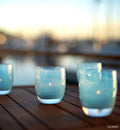 ocean light blue hand-blown glass votive candle holders on an outdoor dark brown patio.