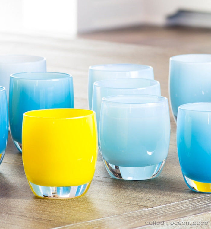 ocean light blue hand-blown glass votive candle holders with daffodil and cabo on a light wood surface.