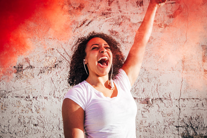 Model is yelling with a red smoke bomb while wearing white Omen wireless earbuds