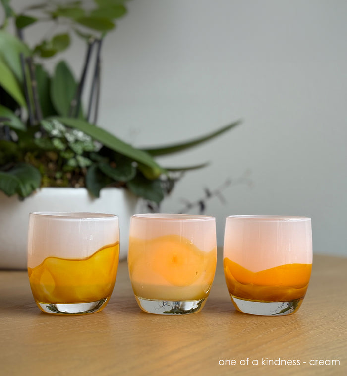 Three yellow and cream coloration glass candle holders  on a wooden surface with a plant in the background.
