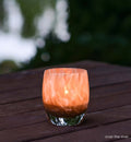 over the river, gold glitter swirled petals, hand-blown glass votive candle holder lit on an outdoor wood table.