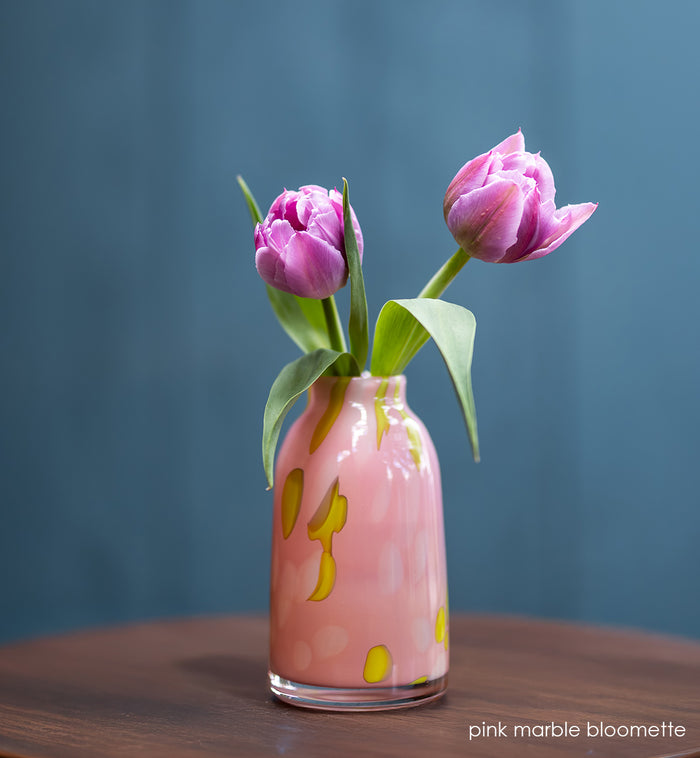 Pink marble-patterned bloomette vase with two purple tulips on a wooden surface and blue background