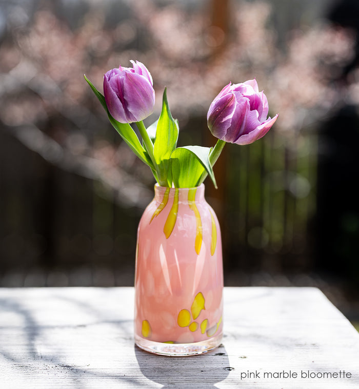 Pink marble-patterned bloomette vase with purple tulips on a wooden surface