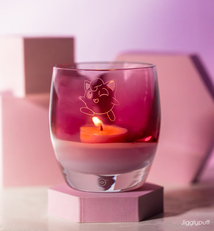 Pink candle holder with Jigglypuff design containing a lit candle on a pink platform.