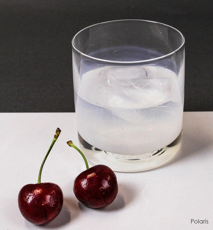 Polaris rocker, clear white hand-blown lowball glass on a white surface next to two cherries.