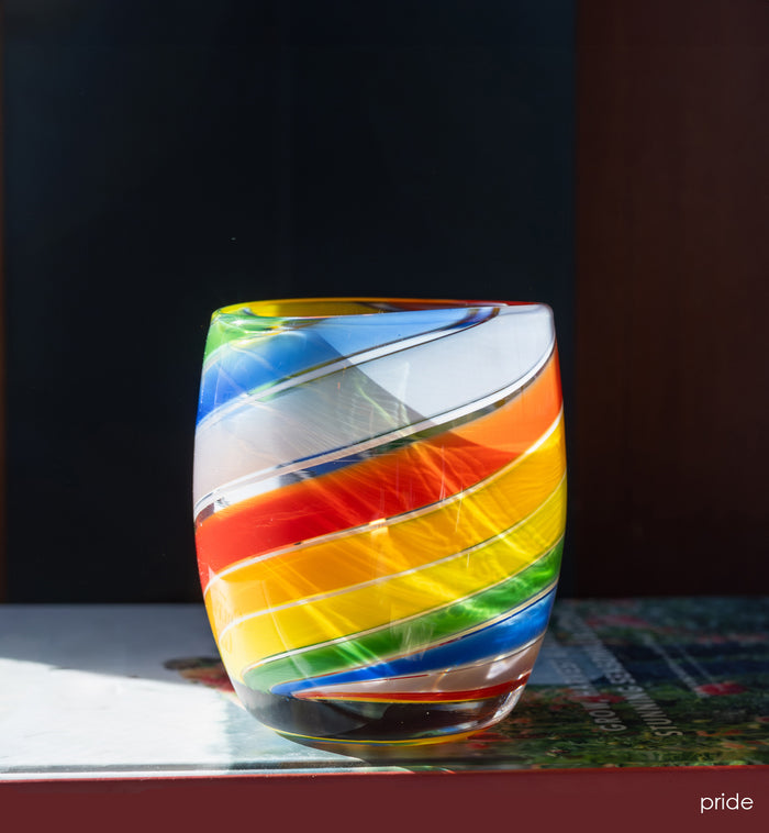 'pride' glassybaby with rainbow swirls, hand-blown glass candle holder sitting on a book