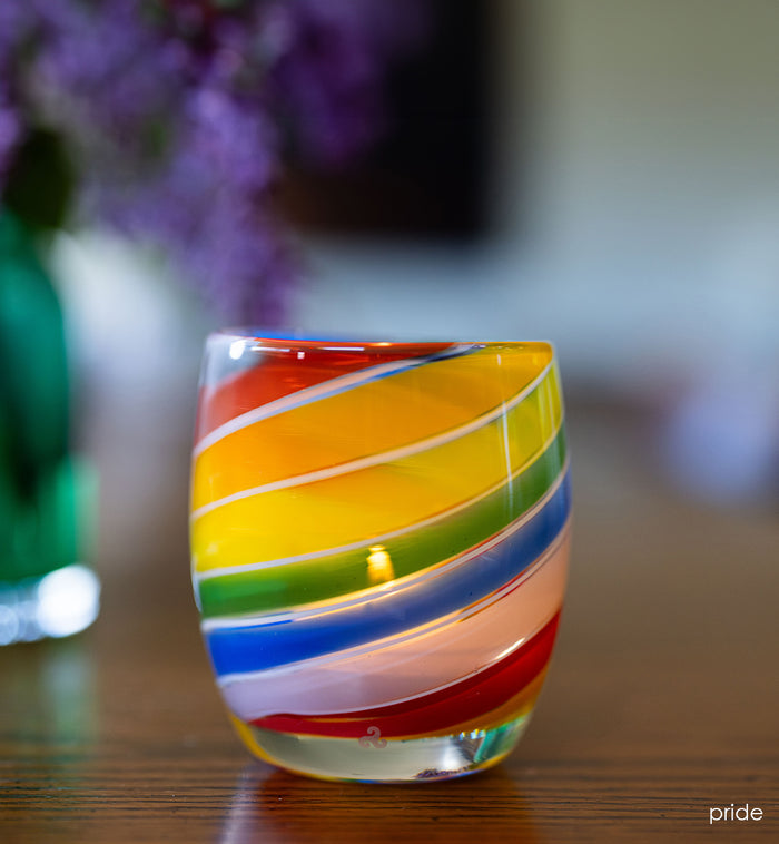'pride' glassybaby with rainbow swirls, hand-blown glass candle holder sitting on wood table