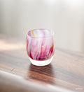 prima pink multi-colored petal, hand-blown glass votive candle holder on a wood surface.