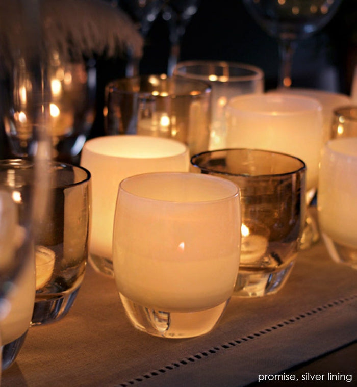 promise cream hand-blown glass votive candle holder lit with silver lining on a dining room table runner.