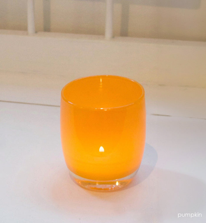 pumpkin orange hand-blown glass votive candle holder with a lit tealight on a white surface.