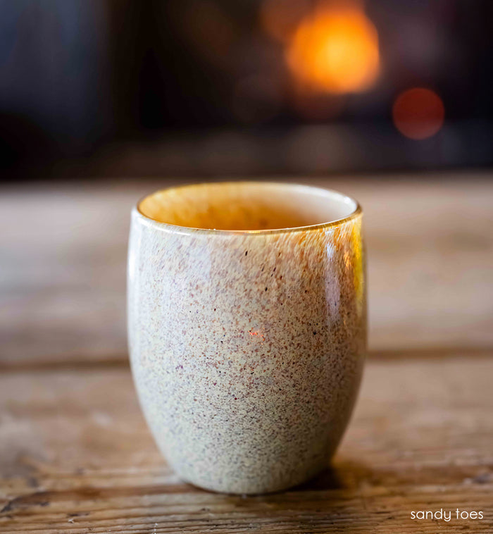 tan, orange, and brown specs covering hand-blown glass candle holder on wood surface