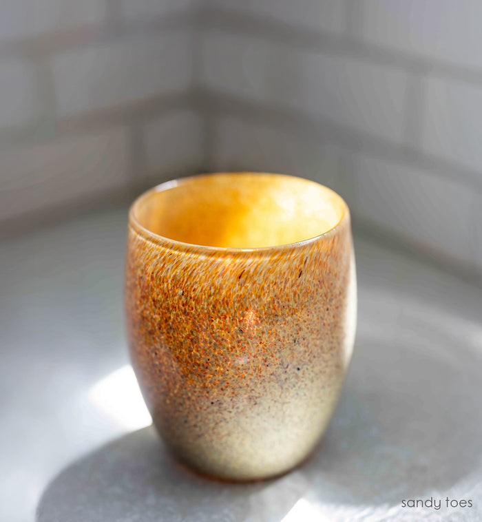 tan, orange, and brown specs covering hand-blown glass candle holder on white surface