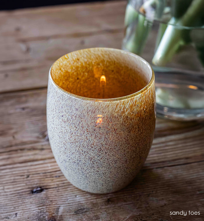tan, orange, and brown specs covering hand-blown glass candle holder on wood surface