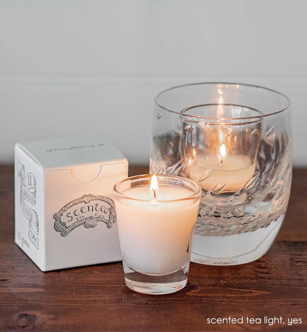 two glassybaby scented tealights, one lit in yes, the other sitting next to yes on wood table with scented tealight box.