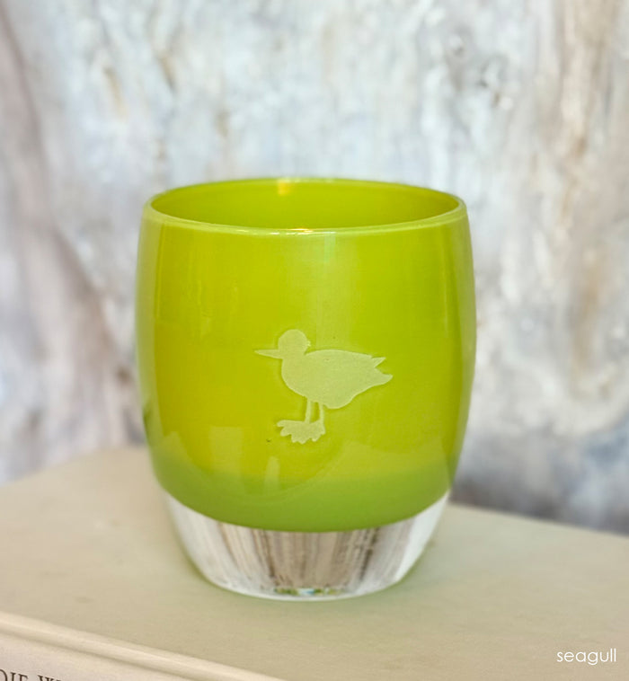 Green glass candle holder with a hand-etched seagull on a white surface