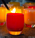 seattle sunset, bright orange red, hand-blown glass votive candle holder on a rocky material table with other votives being lit in background.