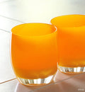 two shine hand-blown bright orange glass votive candle holders on a cream tiled table.