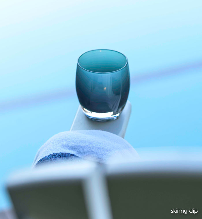 skinny dip, dark teal hand-blown glass votive candle holder perched on a pool chair next to a beach towel.