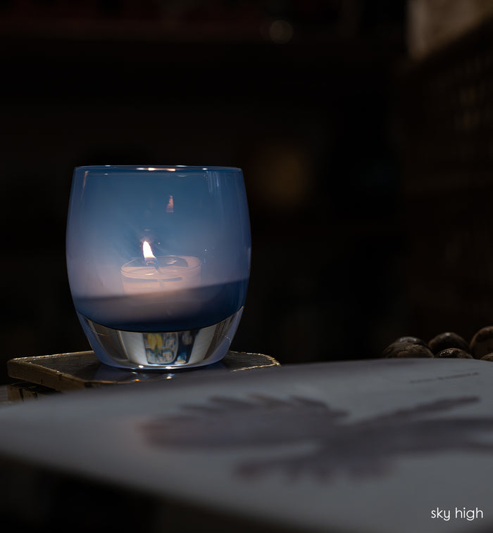 sky high blue hand-blown glass votive candle holder lit in a dark room on a crystal coaster.