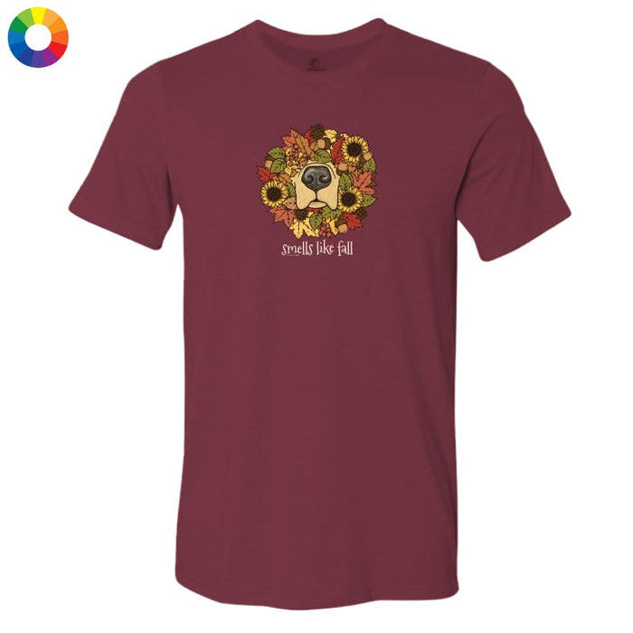 A maroon short-sleeve crewneck t-shirt featuring a graphic of a dog's face surrounded by autumn leaves and sunflowers, with the text 'smells like fall' printed below. A small multicolor color wheel icon is visible in the top-left corner.