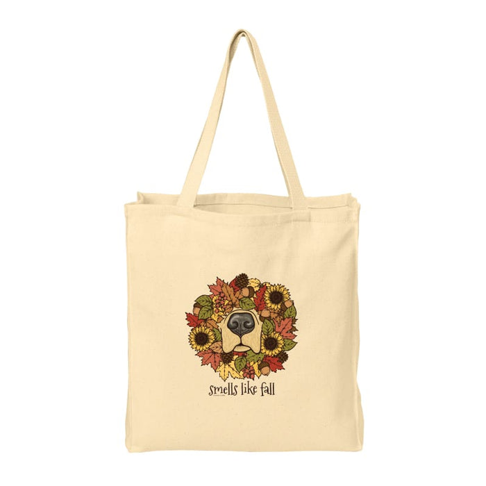 A natural beige canvas tote bag with two shoulder straps, featuring a central graphic of a dog's face framed by a colorful autumn wreath of sunflowers and leaves, with the text 'smells like fall' printed below.