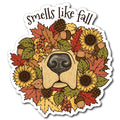 A die-cut sticker featuring a stylized dog face surrounded by autumn leaves, sunflowers, acorns, pinecones, and berries, with the text 'smells like fall' above, shown on a plain white background.
