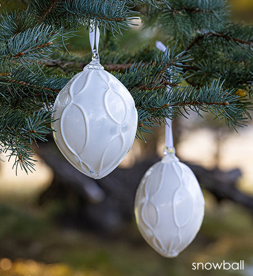snowball white hand-blown glass ornament by glassybaby hanging in pine tree.