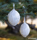 snowball white hand-blown glass ornament by glassybaby hanging in pine tree.