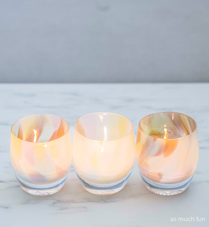 three so much fun, pastel mix, hand-blown glass votive candle holders on a marble surface.