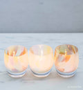 three so much fun, pastel mix, hand-blown glass votive candle holders on a marble surface.