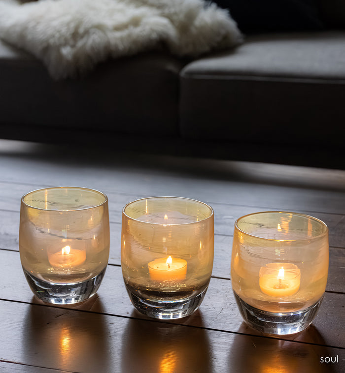 three 'sou' a light yellow transparent glass candle holders with a lit candle on woof table