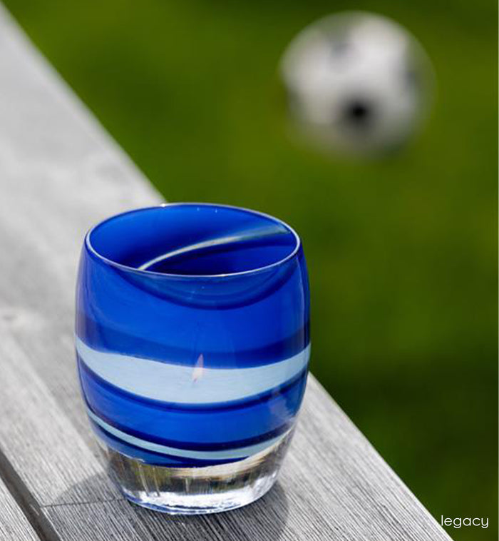 Blue and white striped handblown glass candle holder on a wooden surface with a blurred background with soccer ball
