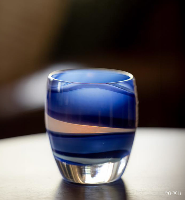Blue and white striped handblown glass candle holder on a wooden surface with a blurred background