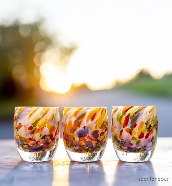 group of 'spontaneous' colorful hand-blown glass candle holder with sunshine behind it