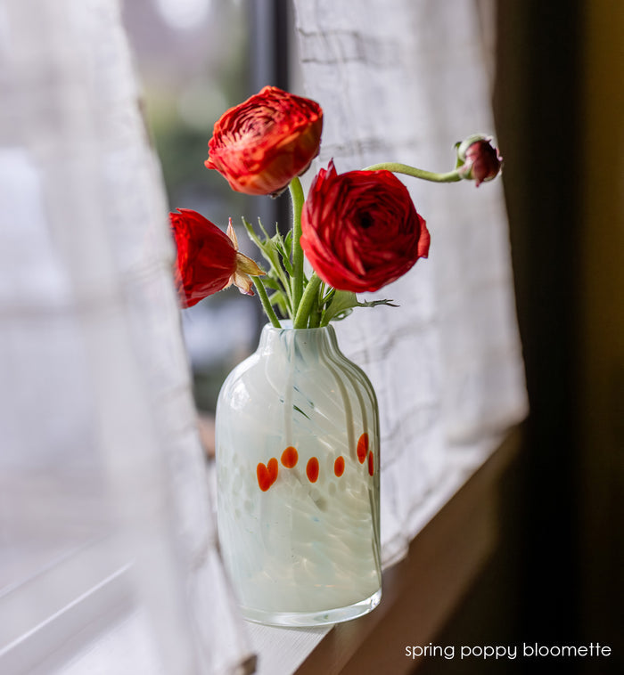 white bloomette vase with red spots with red flowers on a windowsill