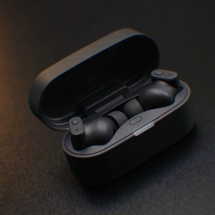 A pair of Status Audio Pro X True Wireless - GoldenSound Edition earbuds rest in an open charging case on a dark, textured surface.