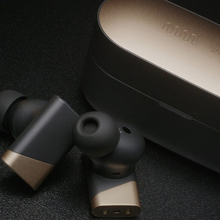 Close-up of the Status Audio Pro X True Wireless - GoldenSound Edition earbuds in sleek black and gold, resting beside their matching charging case from Status Audio on a textured black surface.