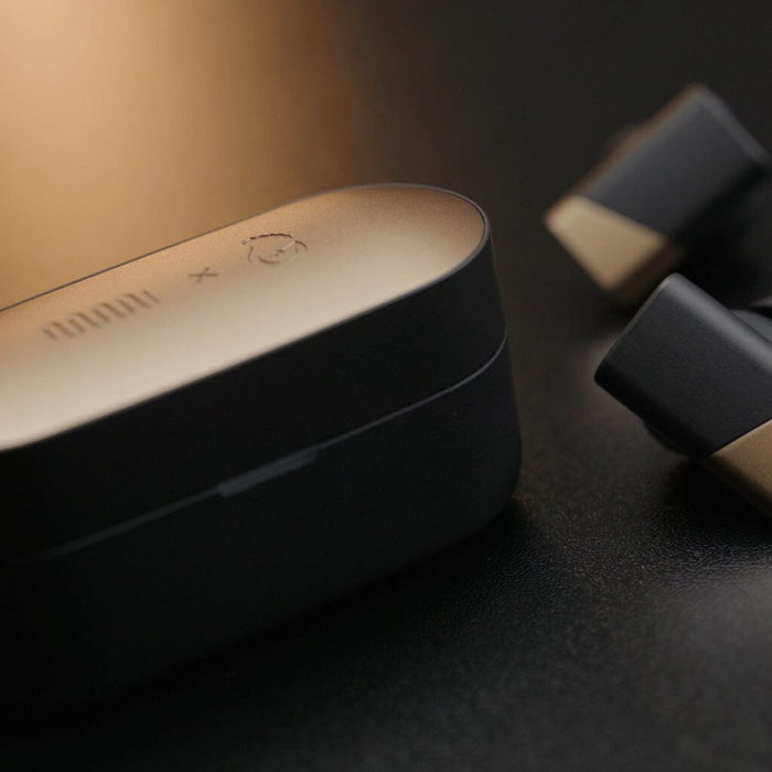 A close-up showcases the Status Audio Pro X True Wireless – GoldenSound Edition case in elegant gold and black, accompanied by two matching earbuds on a dark surface. This limited-edition release from Status Audio captivates with its luxurious design and premium presence.
