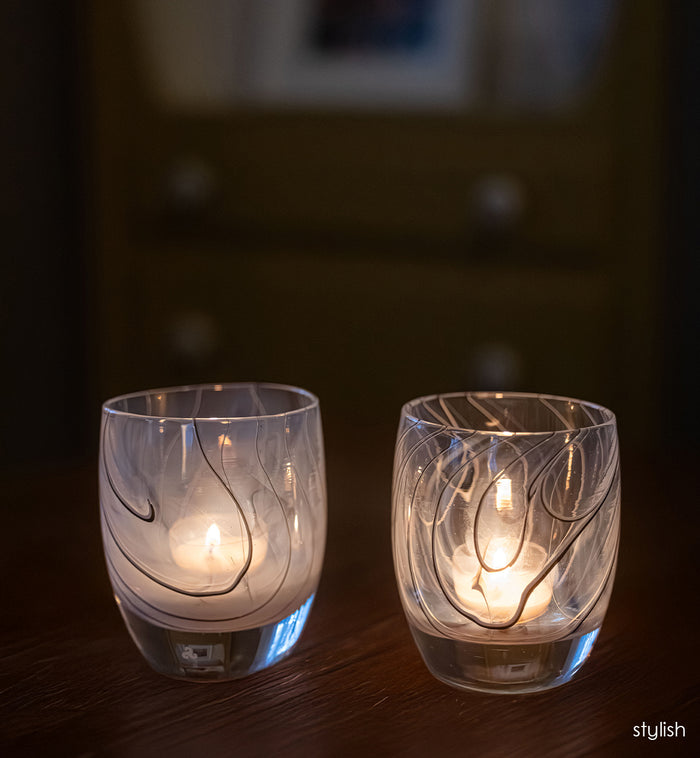 Two lit candle holders with subtle black line designs on a dark background