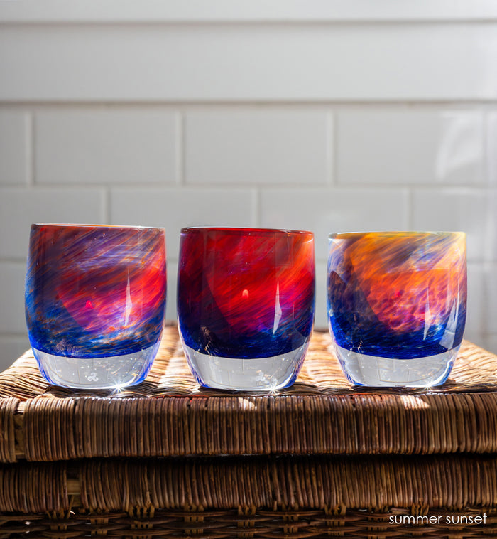 three 'summer sunset' glassybaby | red, yellow, and blue hand-blown glass candle holder on wicker table