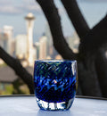 survivor sapphire blue bubble, hand-blown glass votive candle holder sitting on circular table in front of a blurred tree and Seattle space needle and skyline background.